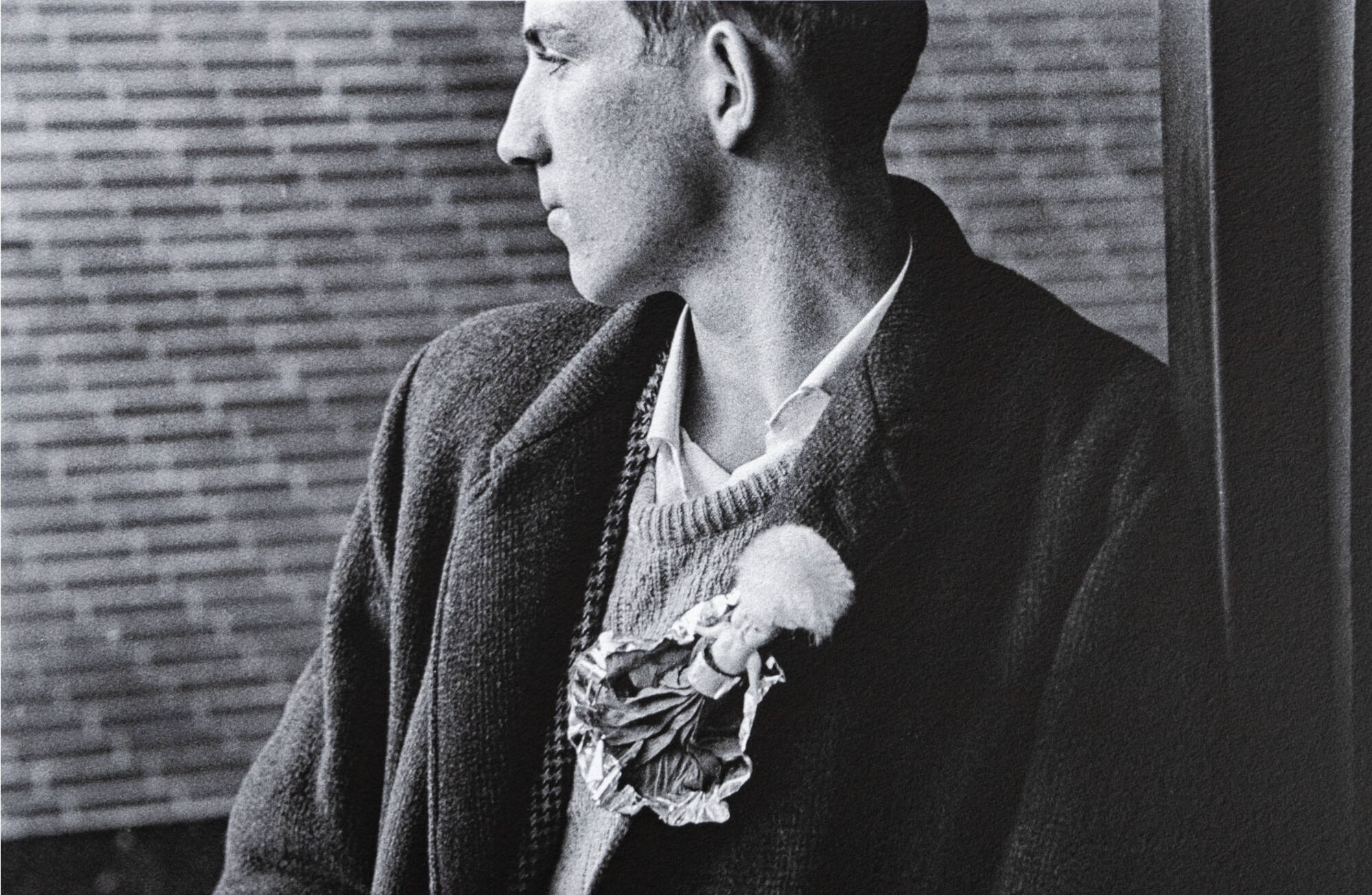 Black and white photograph of a man turned to look out a window. He wears a large brooch.